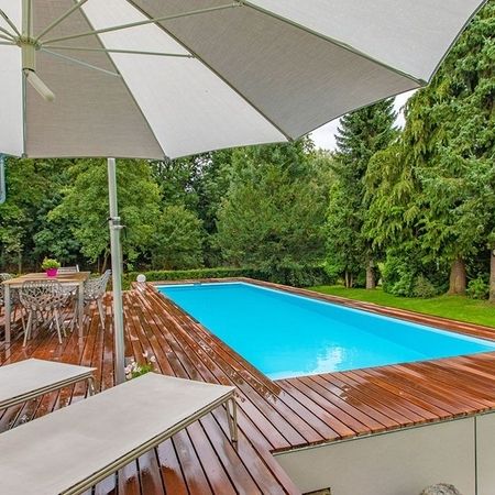 Großer Pool mit einer Holzverkleidung und einem Sonnenschirm