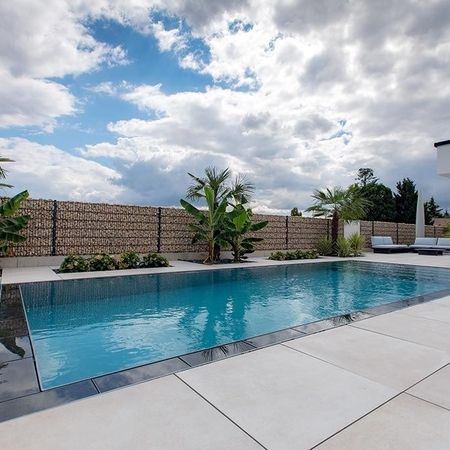 Moderner Pool vor einem weißen Haus und einem Holzzaum